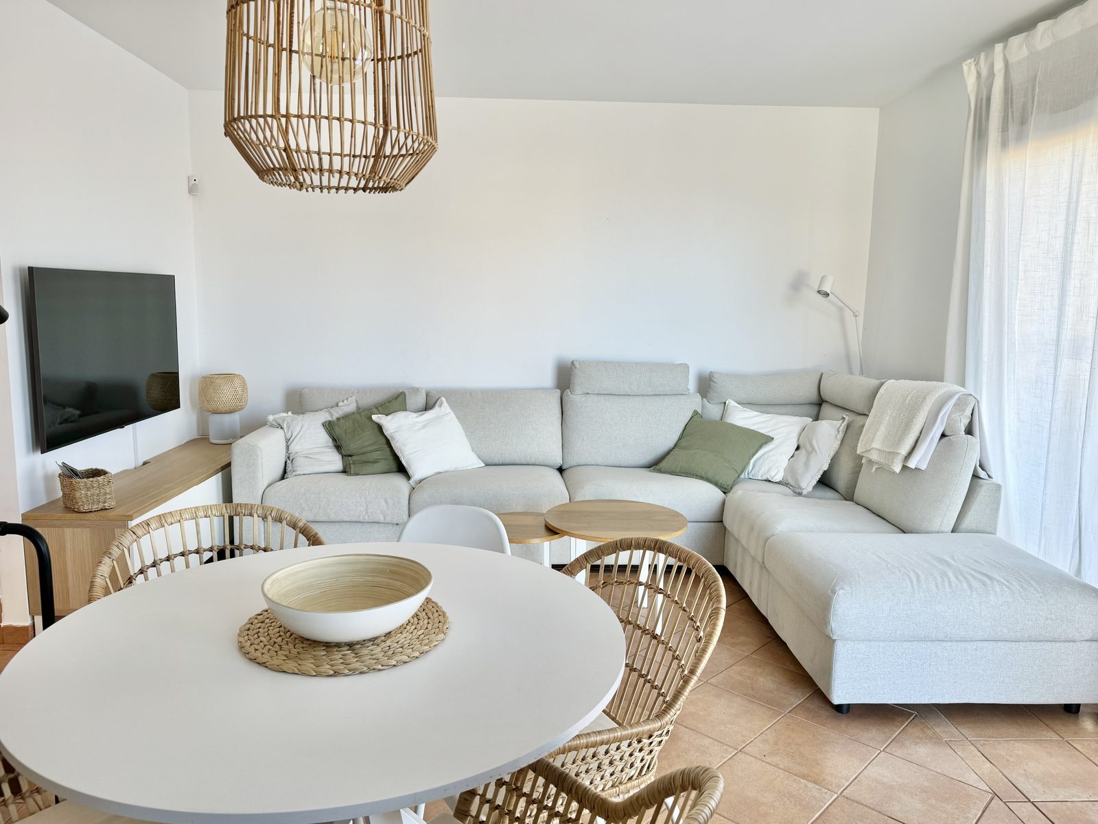 Salón y comedor de Villa Majanicho Inside, con sofá rinconera y mesa redonda de ratán