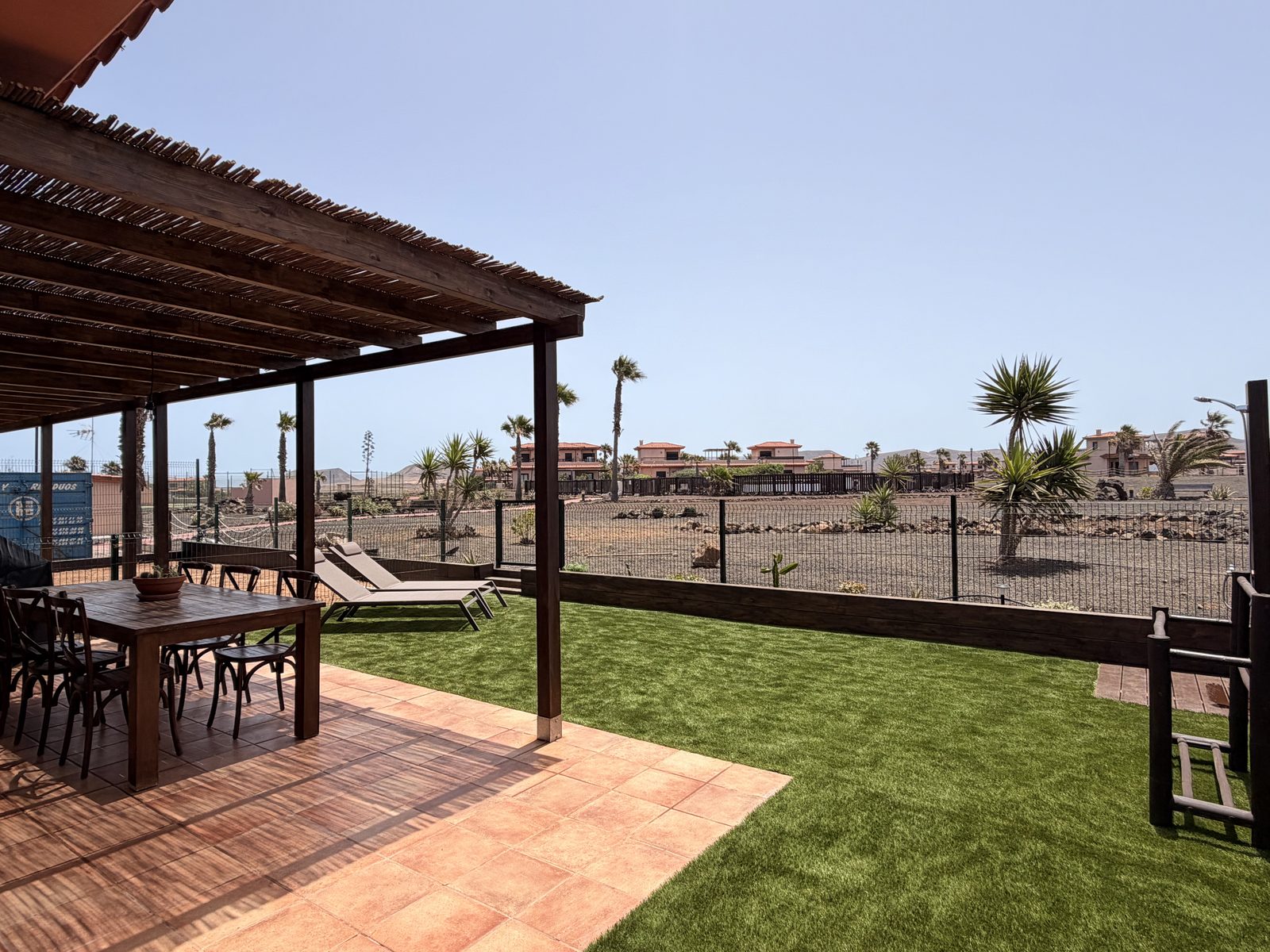 Pérgola, mesa y jardín de césped de Villa Majanicho Origomare, con las palmeras y las montañas al fondo